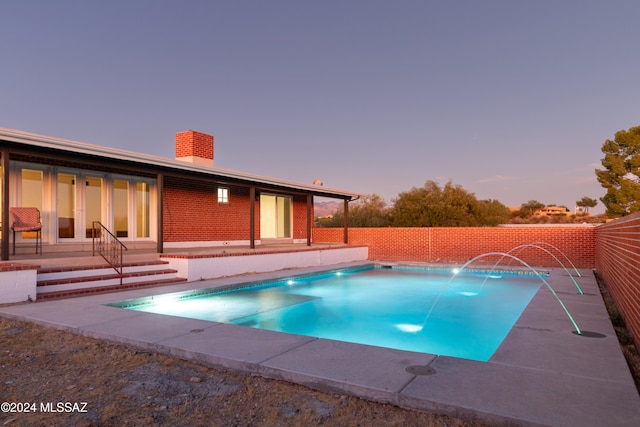 pool at dusk with a patio area and pool water feature