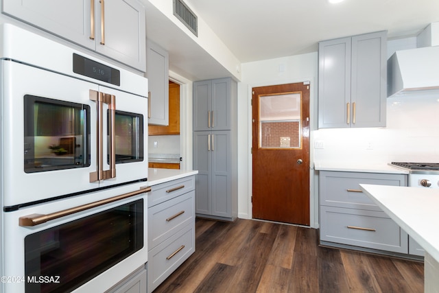 kitchen with wall chimney exhaust hood, dark wood-type flooring, gray cabinetry, stainless steel appliances, and tasteful backsplash