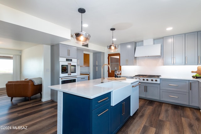 kitchen featuring sink, backsplash, pendant lighting, dark wood-type flooring, and a center island with sink