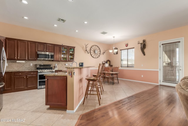 kitchen featuring light stone counters, appliances with stainless steel finishes, a breakfast bar, light hardwood / wood-style flooring, and decorative light fixtures