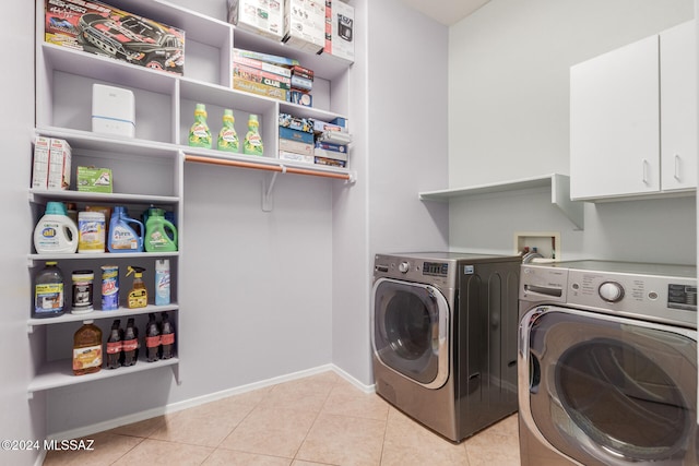 clothes washing area with washing machine and dryer, light tile patterned floors, and cabinets