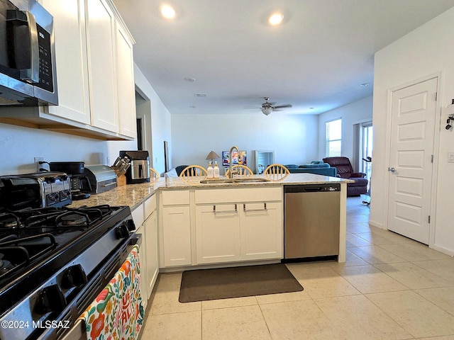 kitchen with light stone countertops, appliances with stainless steel finishes, sink, kitchen peninsula, and white cabinets