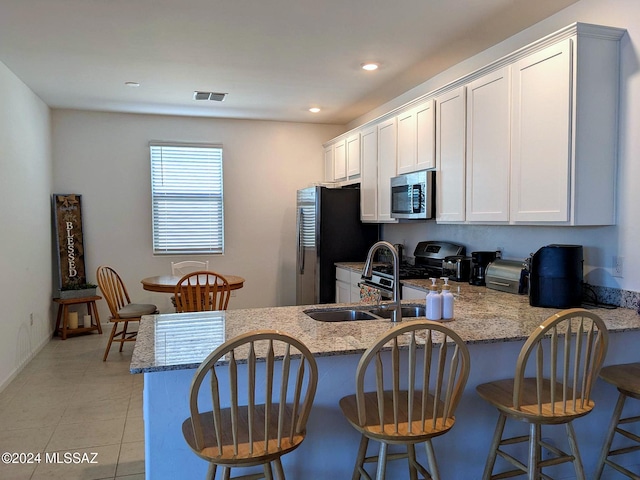 kitchen with light stone counters, appliances with stainless steel finishes, kitchen peninsula, and white cabinetry