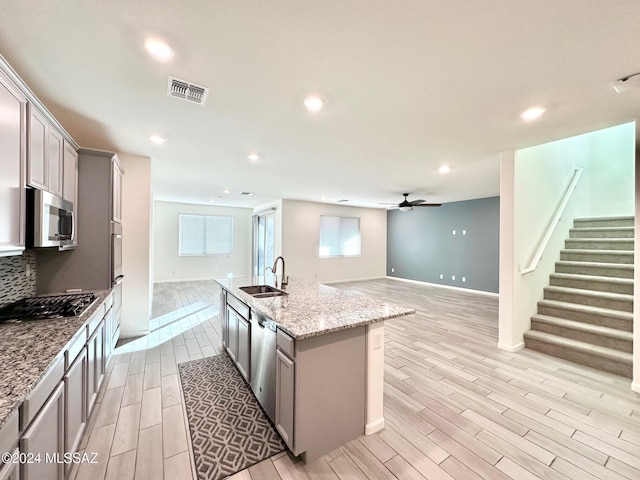 kitchen featuring light stone counters, stainless steel appliances, an island with sink, and gray cabinetry