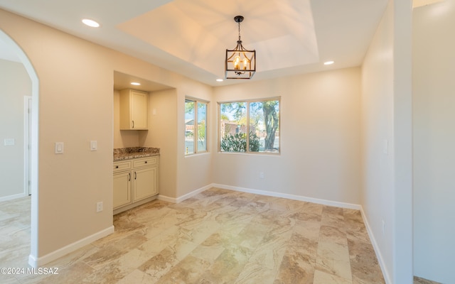 unfurnished dining area featuring a notable chandelier and a raised ceiling