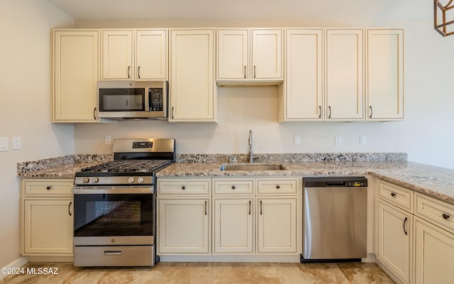 kitchen with light stone countertops, sink, appliances with stainless steel finishes, and cream cabinetry