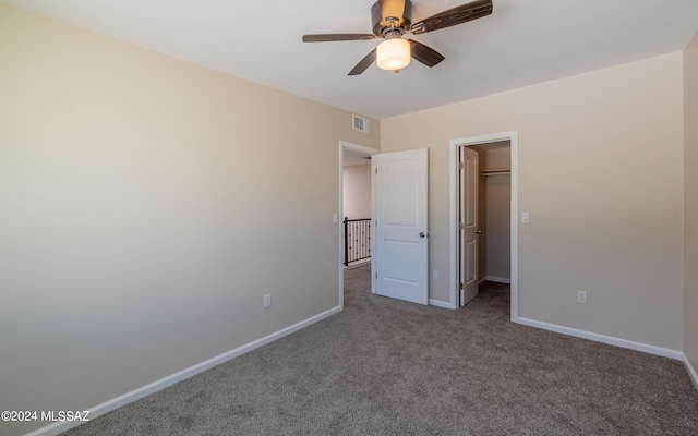 unfurnished bedroom featuring a closet, ceiling fan, carpet flooring, and a walk in closet