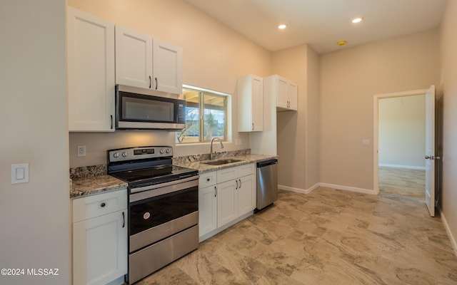 kitchen with white cabinetry, light stone counters, stainless steel appliances, and sink