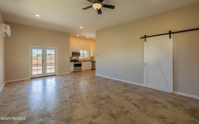 unfurnished living room featuring french doors, ceiling fan, an AC wall unit, and a barn door