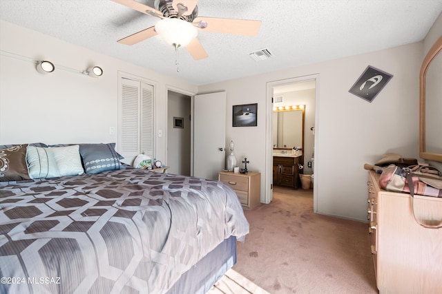 bedroom with ceiling fan, a textured ceiling, a closet, ensuite bath, and light colored carpet