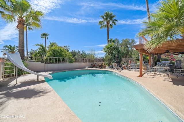 view of swimming pool with a patio area, a water slide, and ceiling fan