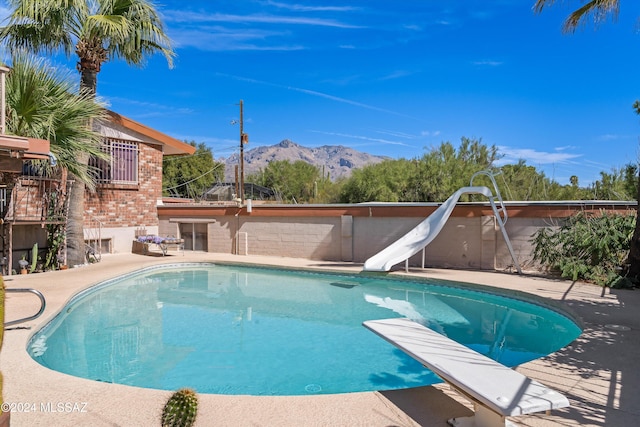 view of pool with a water slide, a mountain view, and a diving board