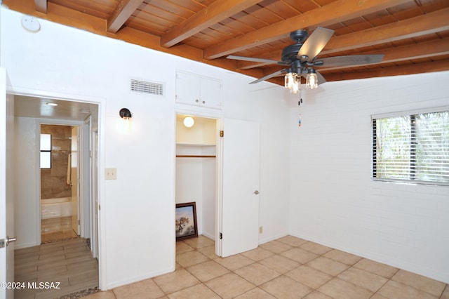 unfurnished bedroom featuring vaulted ceiling with beams, wood ceiling, a walk in closet, light tile patterned floors, and ceiling fan