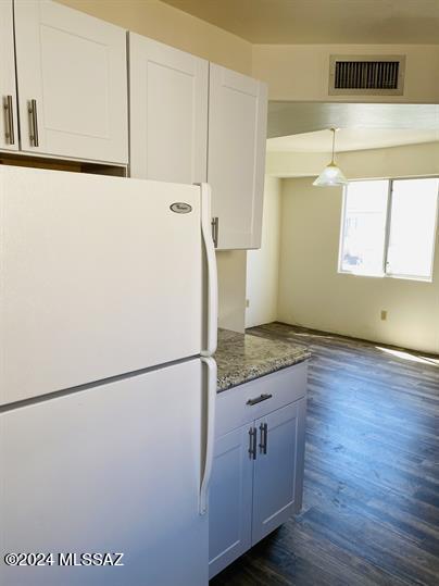 kitchen with dark wood-type flooring, dark stone counters, pendant lighting, white cabinetry, and white fridge