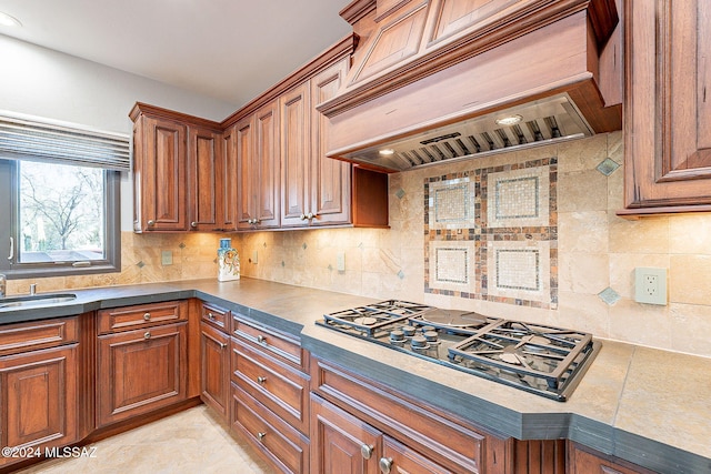 kitchen with sink, custom exhaust hood, decorative backsplash, and stainless steel gas stovetop