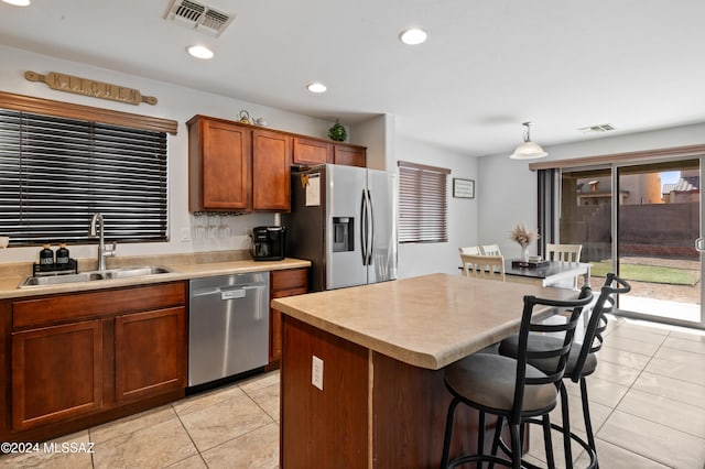 kitchen featuring light tile patterned flooring, stainless steel appliances, sink, decorative light fixtures, and a center island