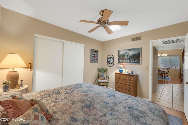 bedroom featuring light tile patterned floors, visible vents, a closet, and ceiling fan with notable chandelier