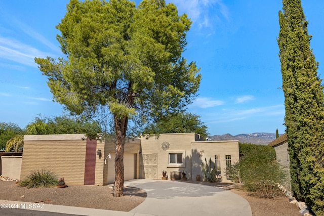 pueblo revival-style home with driveway, an attached garage, a mountain view, and stucco siding