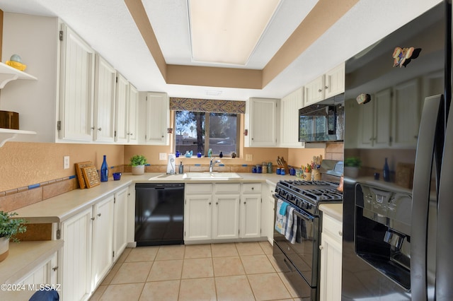 kitchen featuring a tray ceiling, light tile patterned floors, light countertops, a sink, and black appliances