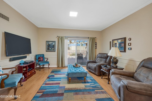 living area with light wood-type flooring, a wainscoted wall, visible vents, and crown molding