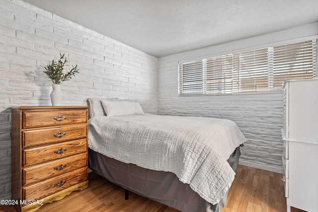 bedroom with hardwood / wood-style flooring and brick wall