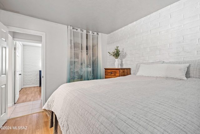 bedroom featuring light hardwood / wood-style floors and brick wall