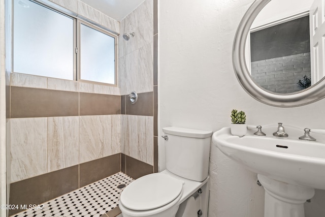 bathroom with toilet, sink, and a tile shower