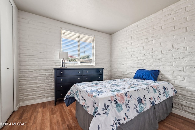 bedroom featuring dark wood-type flooring and brick wall