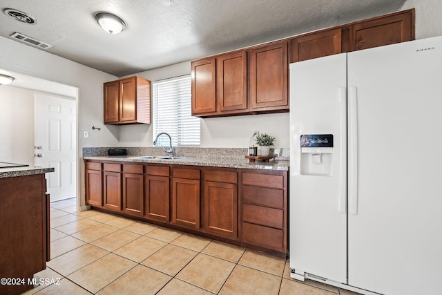 kitchen featuring a textured ceiling, white fridge with ice dispenser, light tile patterned floors, and sink