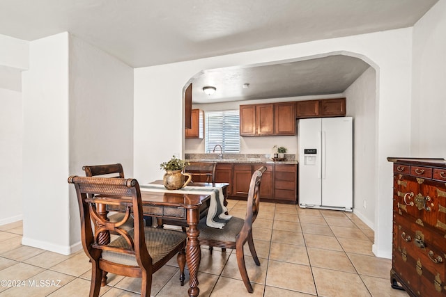 kitchen with light tile patterned floors, stone countertops, sink, and white refrigerator with ice dispenser