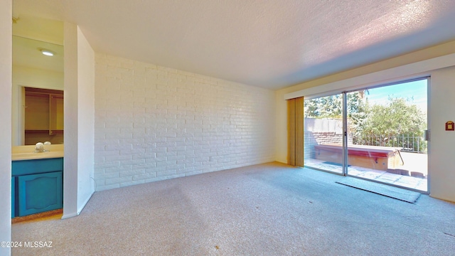 carpeted empty room featuring brick wall and a textured ceiling