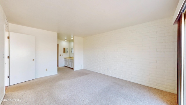 unfurnished bedroom with light colored carpet, brick wall, and ensuite bathroom