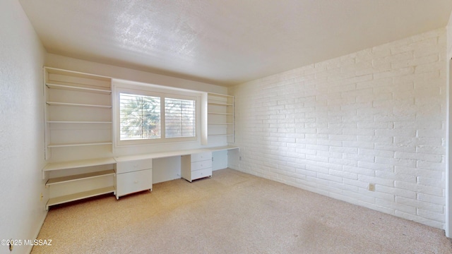 unfurnished office featuring a textured ceiling, brick wall, built in study area, and light colored carpet