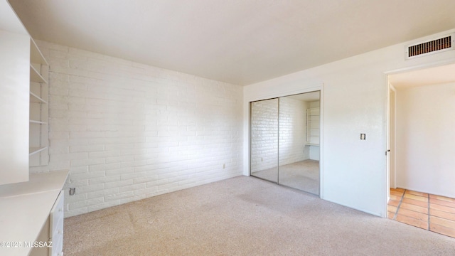 unfurnished bedroom featuring a closet, visible vents, light carpet, and brick wall