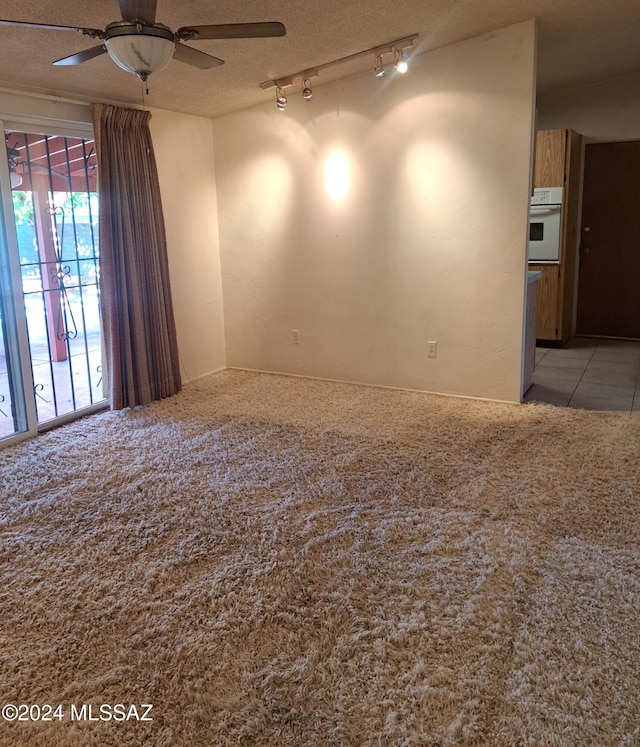 carpeted empty room featuring ceiling fan, track lighting, and a textured ceiling