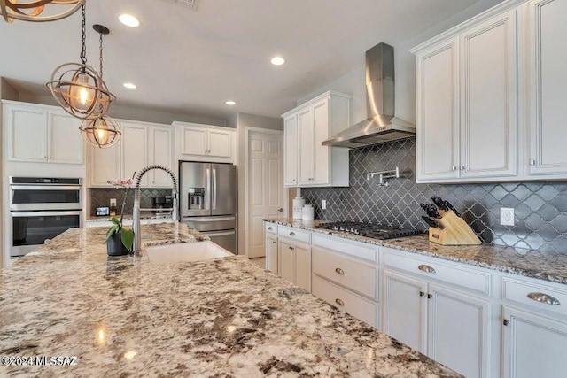 kitchen with wall chimney range hood, white cabinets, hanging light fixtures, backsplash, and stainless steel appliances