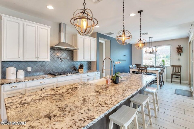 kitchen featuring stainless steel gas stovetop, white cabinets, wall chimney range hood, and pendant lighting