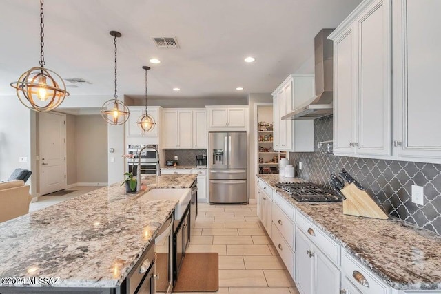 kitchen featuring wall chimney range hood, a spacious island, white cabinetry, stainless steel appliances, and decorative light fixtures