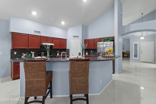 kitchen featuring a kitchen bar, a kitchen island with sink, stainless steel fridge with ice dispenser, and high vaulted ceiling