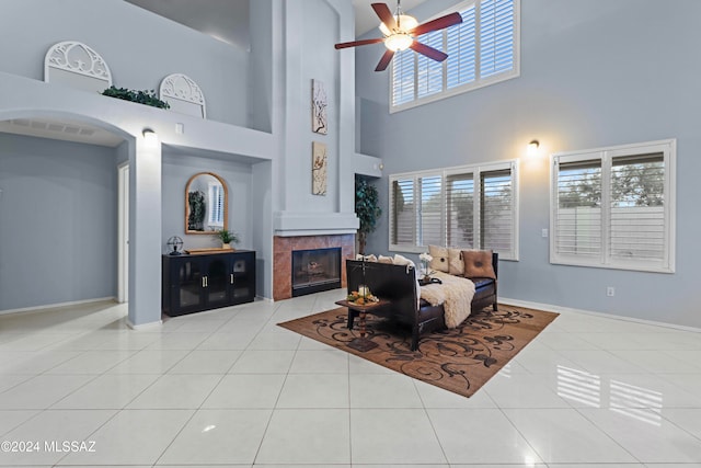 tiled living room featuring a towering ceiling, a fireplace, and ceiling fan