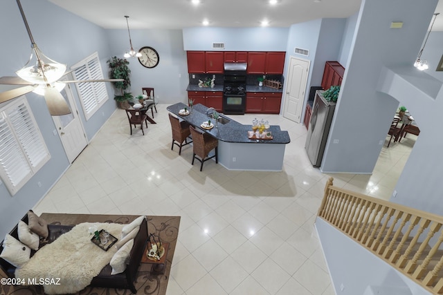 kitchen with tasteful backsplash, light tile patterned floors, black stove, ceiling fan with notable chandelier, and a towering ceiling