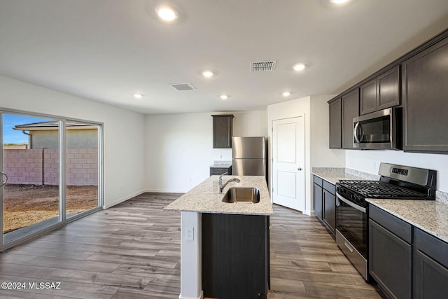 kitchen with stainless steel appliances, sink, hardwood / wood-style floors, dark brown cabinets, and a kitchen island with sink