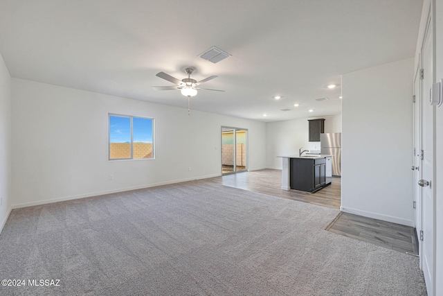 unfurnished living room with sink, ceiling fan, and light hardwood / wood-style flooring