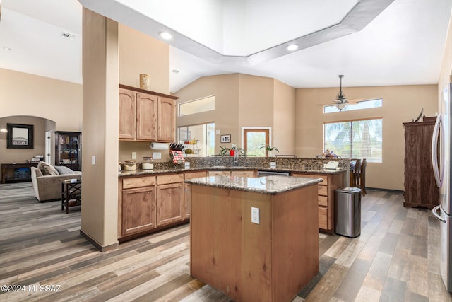 kitchen with ceiling fan, kitchen peninsula, dark stone countertops, wood-type flooring, and a kitchen island