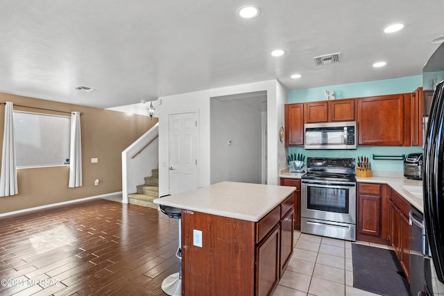 kitchen with light wood-type flooring, appliances with stainless steel finishes, a center island, and a breakfast bar