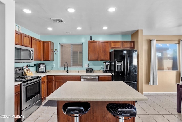 kitchen featuring a kitchen bar, stainless steel appliances, sink, light tile patterned floors, and a kitchen island