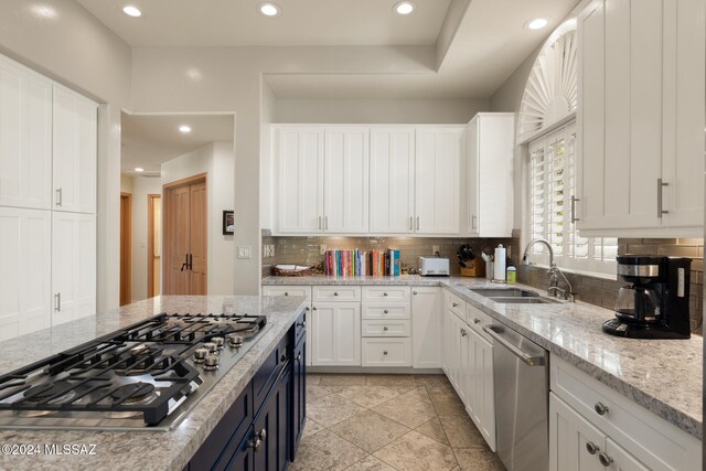 kitchen with sink, stainless steel appliances, white cabinets, light stone counters, and decorative backsplash