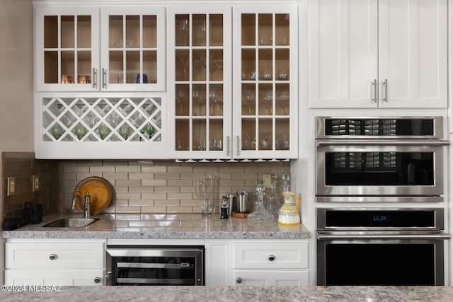 kitchen with decorative backsplash, white cabinets, wine cooler, double oven, and light stone counters