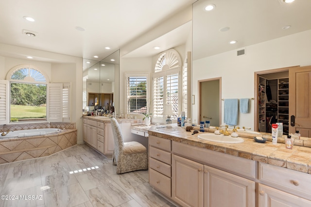 bathroom featuring vanity, a healthy amount of sunlight, and tiled bath