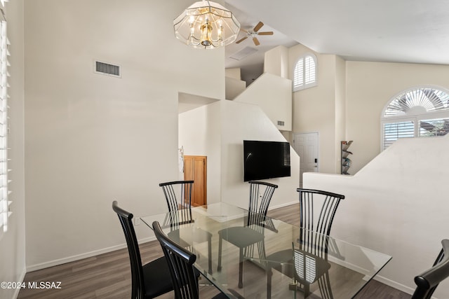 dining room featuring hardwood / wood-style floors, ceiling fan with notable chandelier, and a towering ceiling